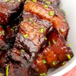 Portrait close up image of sticky gluhwein pork belly bites served with potato wedges and snipped chives