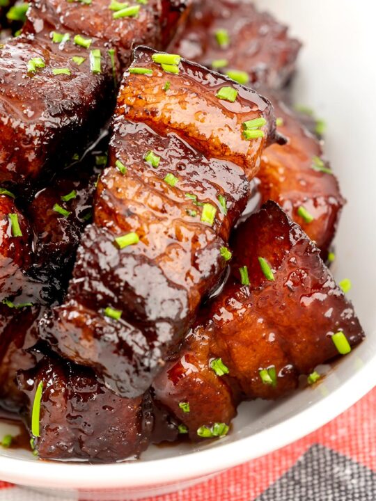 Portrait close up image of sticky gluhwein pork belly bites served with potato wedges and snipped chives