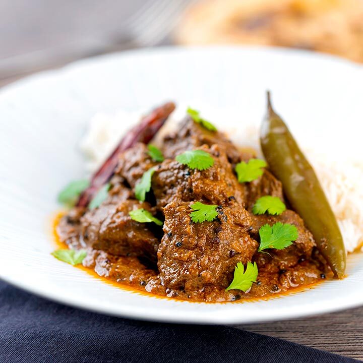 Square image of an achar gosht lamb or mutton curry served on a white plate with whole chilies, basmati rice and coriander leaves