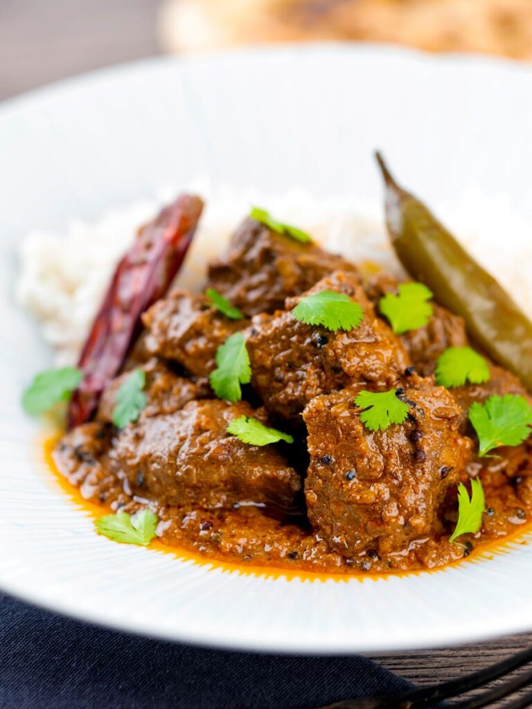 Portrait image of an achar gosht curry served on a white plate with whole chilies, basmati rice
