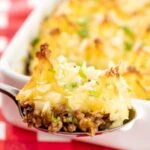 Portrait close up image of a spoonful of cheesy cumberland pie with a whole pie served in a white gratin dish in the background