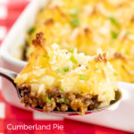 Portrait close up image of a spoonful of cheesy cumberland pie with a whole pie served in a white gratin dish in the background with a title overlay