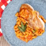 Portrait overhead image of Fagioli all&rsquo;uccelletto or Italian Baked Beans served with a pork loin steak and crispy fried sage leaves