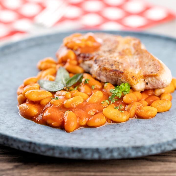 Square image of Fagioli all’uccelletto or Italian Baked Beans served with a pork loin steak and crispy fried sage leaves