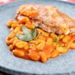 Portrait image of Fagioli all&rsquo;uccelletto or Italian Baked Beans served with a pork loin steak and crispy fried sage leaves