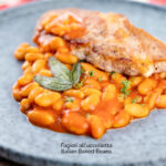 Portrait image of Fagioli all’uccelletto or Italian Baked Beans served with a pork loin steak and crispy fried sage leaves featuring a title overlay