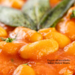 Portrait close up image of Fagioli all’uccelletto or Italian Baked Beans served with a pork loin steak and crispy fried sage leaves featuring a title overlay