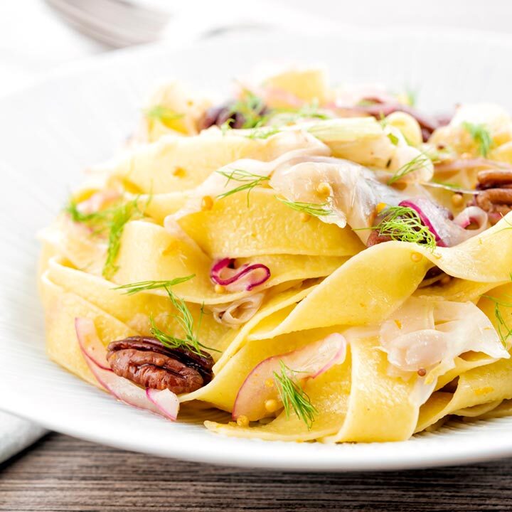 Square image of fennel pasta made with pappardelle served with pecan nuts and red onion served in a white pasta bowl