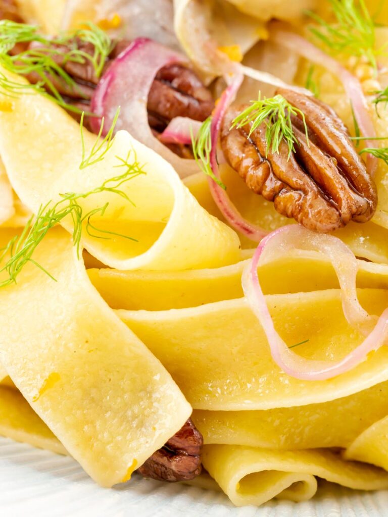 Portrait close up image of fennel pasta made with pappardelle served with pecan nuts and red onion served in a white pasta bowl