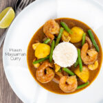 Portrait overhead image of a Thai Prawn Massaman Curry with potatoes and green beans served in a white bowl featuring a text overlay