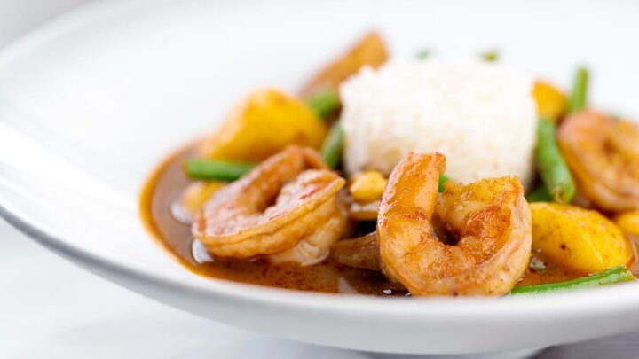 Landscape image of a Thai Prawn Massaman Curry with potatoes and green beans served in a white bowl