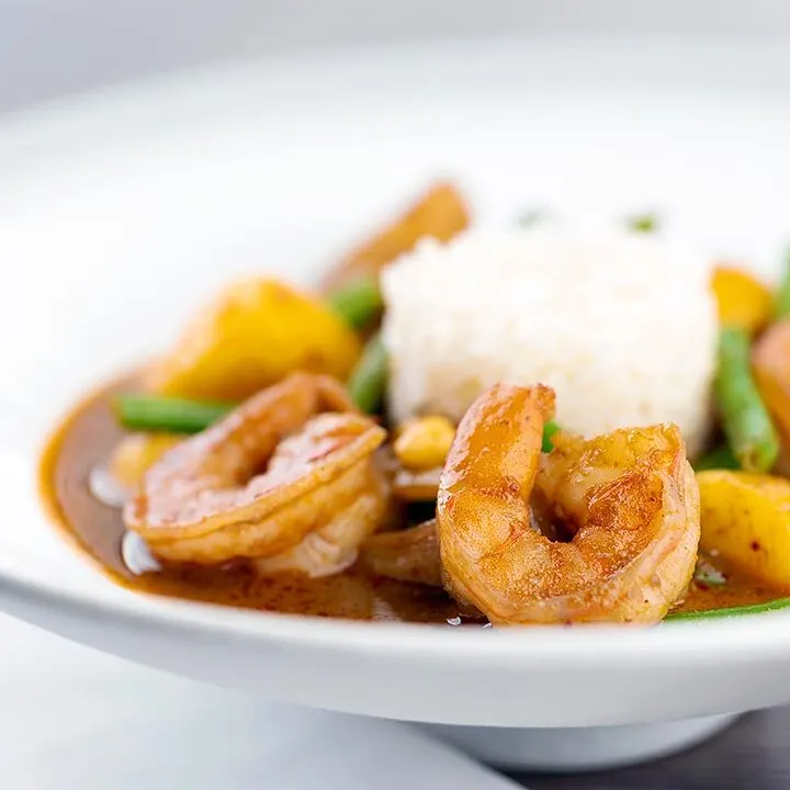 Square image of a Thai Prawn Massaman Curry with potatoes and green beans served in a white bowl