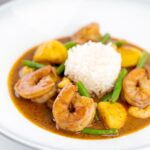 Portrait image of a Thai Prawn Massaman Curry with potatoes and green beans served in a white bowl