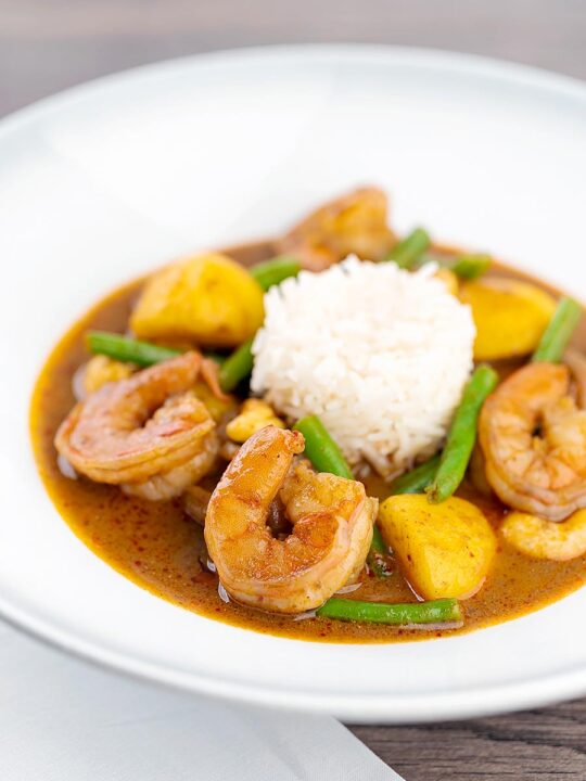 Portrait image of a Thai Prawn Massaman Curry with potatoes and green beans served in a white bowl