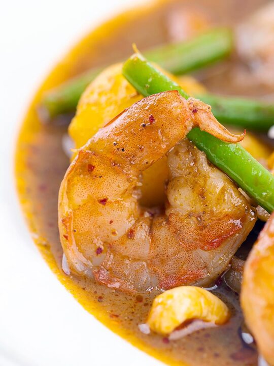 Portrait close up image of a Thai Prawn Massaman Curry with potatoes and green beans served in a white bowl