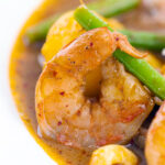 Portrait close up image of a Thai Prawn Massaman Curry with potatoes and green beans served in a white bowl featuring a text overlay