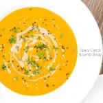 Portrait overhead image of a spicy carrot and lentil soup spiced with harissa paste and garnished with a swirl of tahini served in a white bowl featuring a title overlay