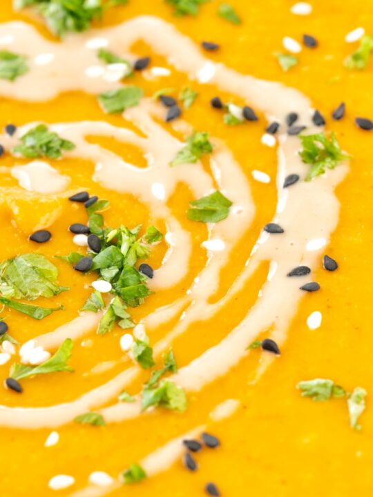 Portrait close up image of a spicy carrot and lentil soup spiced with harissa paste and garnished with a swirl of tahini