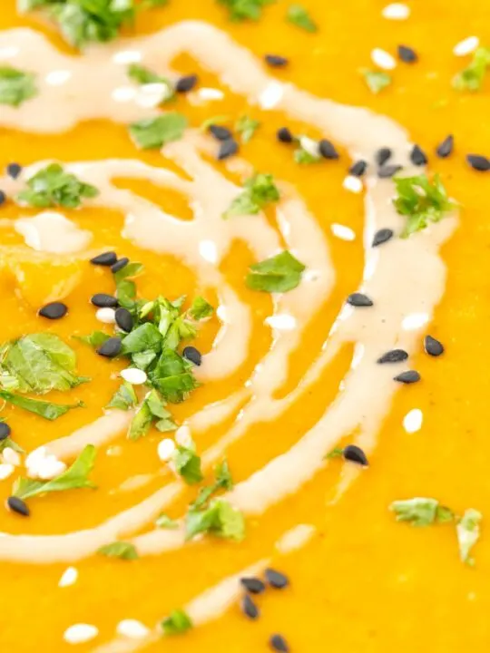 Portrait close up image of a spicy carrot and lentil soup spiced with harissa paste and garnished with a swirl of tahini