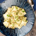 Portrait overhead image of homemade spinach and ricotta ravioli with a lemon caper butter sauce in a blue pasta bowl
