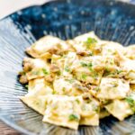 Portrait image of homemade spinach and ricotta ravioli with a lemon caper butter sauce in a blue patterned pasta bowl