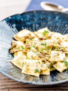 Portrait image of homemade spinach and ricotta ravioli with a lemon caper butter sauce in a blue patterned pasta bowl