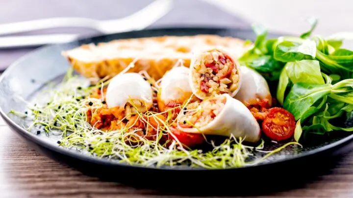 Landscape image of brown rice stuffed squid on a tomato sauce served with ciabatta bread, lambs lettuce and sprouted onion seeds