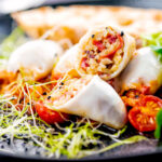 Portrait image of brown rice stuffed squid on a tomato sauce served with ciabatta bread and sprouted onion seeds featuring a title overlay