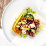 Portrait overhead image of teriyaki tofu served with pak choi, white rice and spring onions on a white plate
