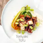 Portrait overhead image of teriyaki tofu served with pak choi, white rice and spring onions on a white plate featuring a title overlay