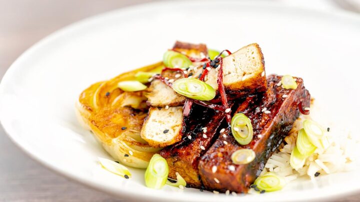 Landscape image of teriyaki tofu served with pak choi, white rice and spring onions on a white plate