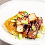 Portrait overhead image of teriyaki tofu served with pak choi, white rice and spring onions on a white plate
