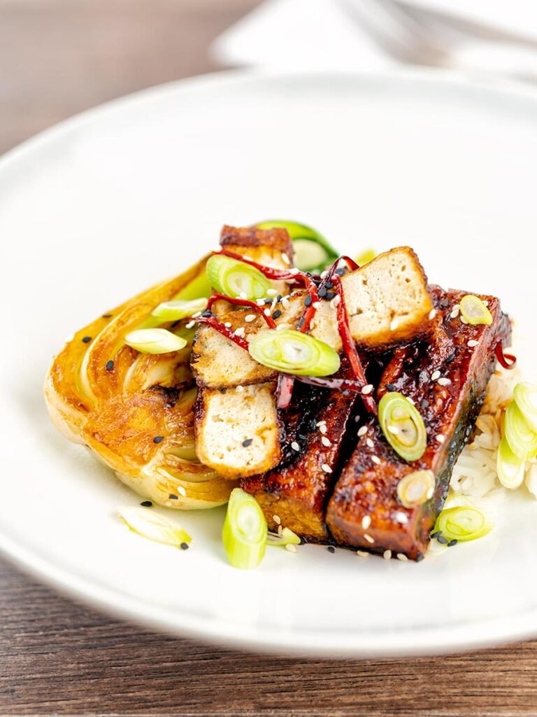Portrait overhead image of teriyaki tofu served with pak choi, white rice and spring onions on a white plate