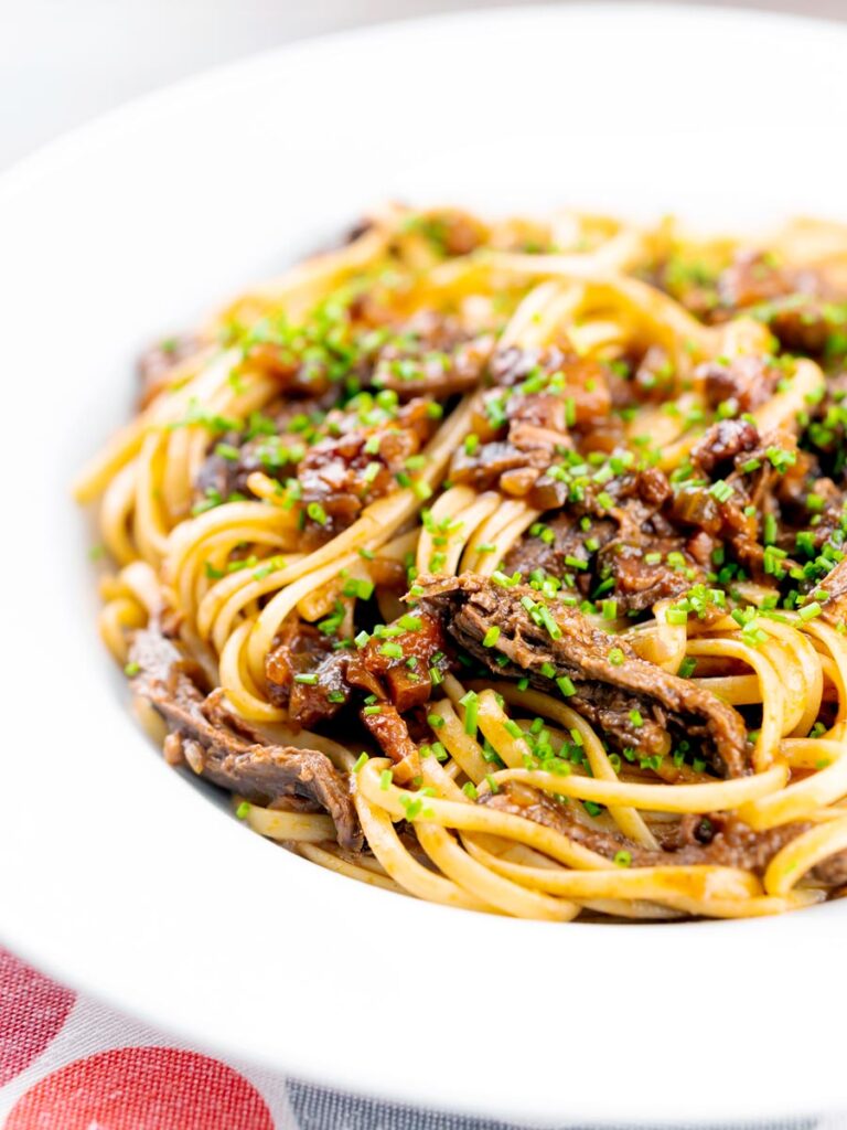 Portrait image of a venison ragu served with linguini pasta garnished with snipped chives and served in a white bowl