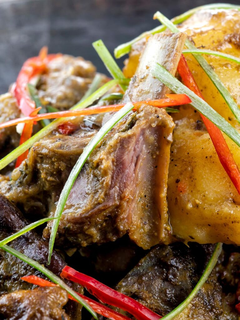 Portrait close up image of Jamaican curry goat with potatoes served with shredded chilli and green onions