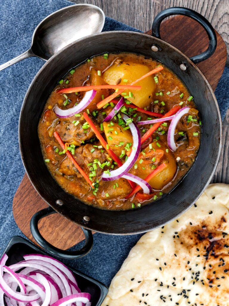 Portrait overhead image of aloo gosht, an Indian lamb or mutton and potato curry served with naan bread and sliced red onions