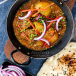 Portrait overhead image of aloo gosht, an Indian lamb or mutton and potato curry served with naan bread and sliced red onions featuring a title overlay