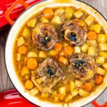 Portrait overhead image of a lamb neck stew using bone in lamb neck chops, potatoes, carrots and parsnips cooked in a red cast iron pan