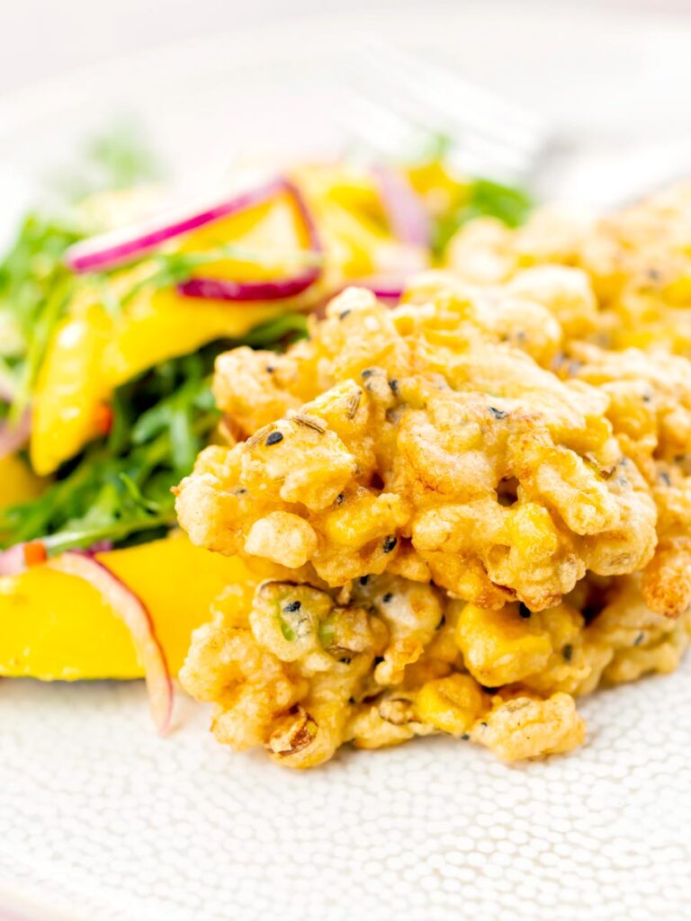 Portrait image of prawn fritters with sweetcorn and spring onion served with a mango salad