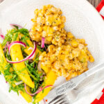 Portrait overhead image of prawn fritters with sweetcorn and spring onion served with a mango salad featuring a title overlay