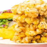 Portrait close up image of prawn fritters with sweetcorn and spring onion served with a mango salad featuring a title overlay