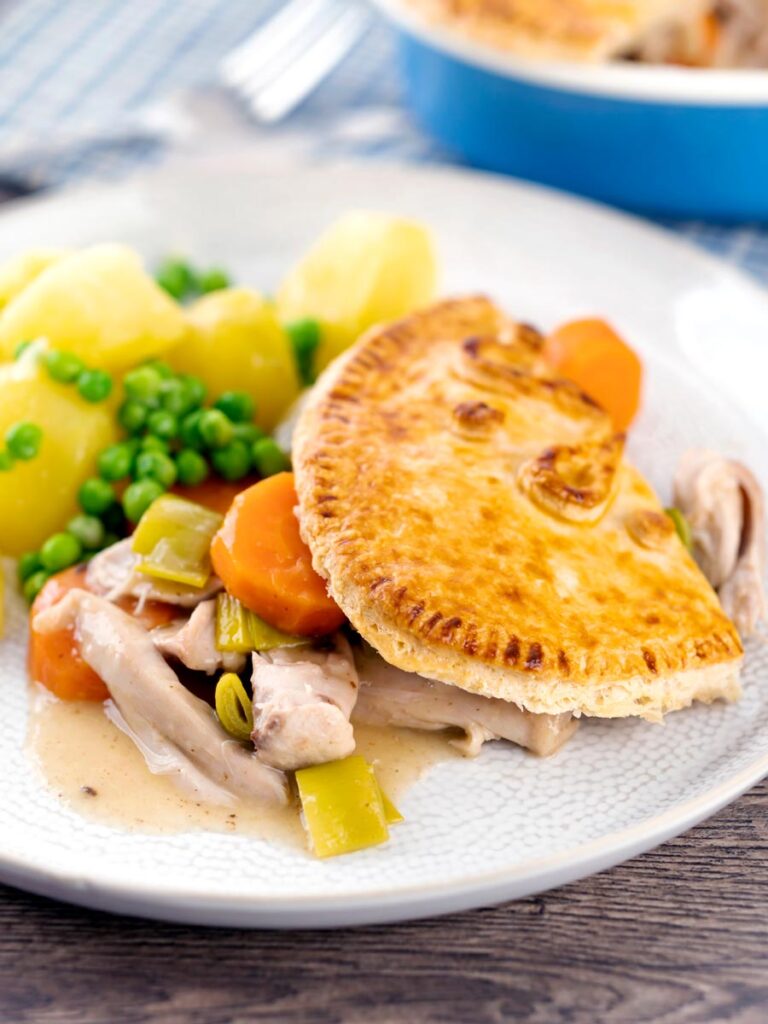 Portrait image of a rabbit pie under a suet crust served on a plate with buttered potatoes and peas
