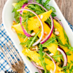 Portrait overhead image of a spicy mango salad with rocket or arugula, shredded red onions and pine nuts featuring a title overlay