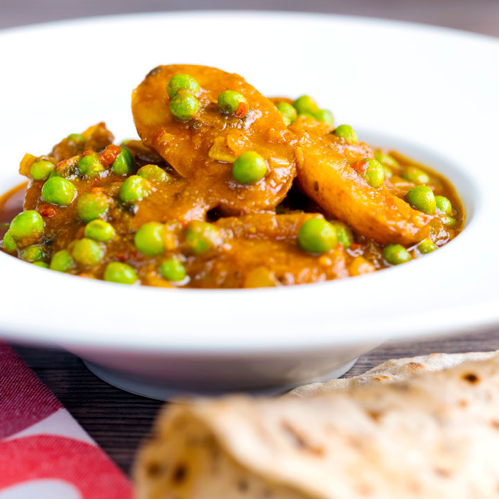 Indian aloo matar, pea and potato curry served in a white bowl with a chapati flatbread.
