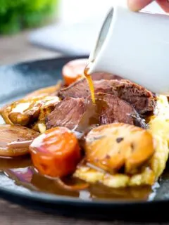 Portrait image of gravy being poured over beer braised beef cheeks with carrot and mushrooms