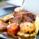 Portrait image of gravy being poured over beer braised beef cheeks with carrot and mushrooms featuring a title overlay