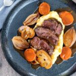 Portrait overhead image of beer braised beef cheeks with carrot, shallot and mushrooms served over mashed potato