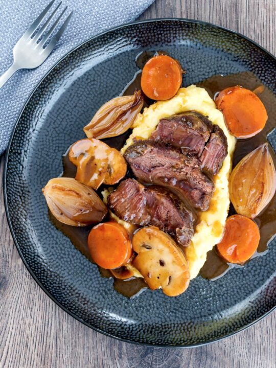 Portrait overhead image of beer braised beef cheeks with carrot, shallot and mushrooms served over mashed potato