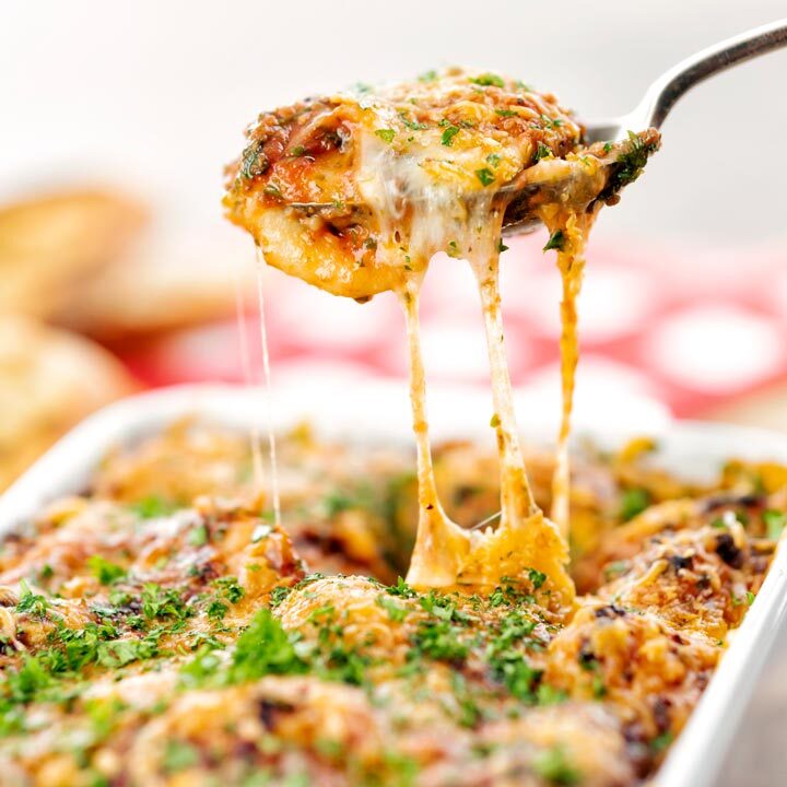 Square close up image of gnocchi alla Sorrentina served in a gratin dish being served with a spoon showing gooey mozzarella cheese strings