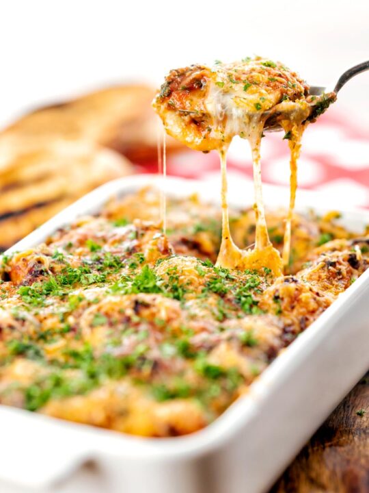 Portrait image of gnocchi alla Sorrentina served in a gratin dish being served with a spoon showing gooey mozzarella cheese strings